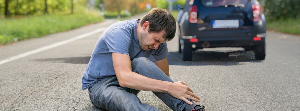Povređeni pešak sedi na trotoaru nakon saobraćajne nezgode