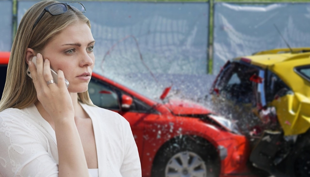 Dva oštećena automobila nakon sudara, dok žena pored vozila poziva pomoć telefonom.